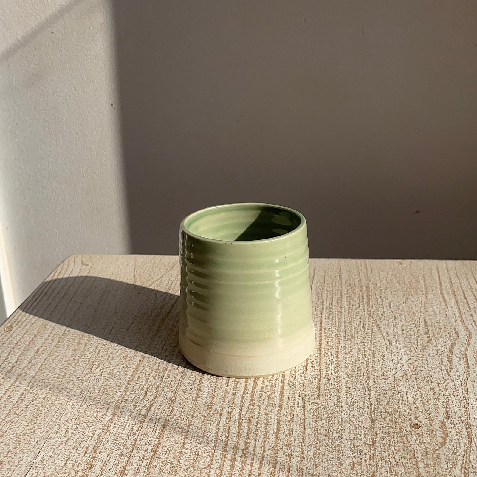 Green ceramic cup on a textured surface with a neutral background
