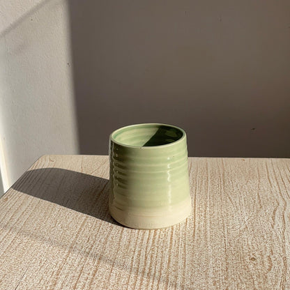 Green ceramic cup on a textured surface with a neutral background
