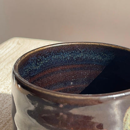 Close-up of a dark ceramic cup with a textured interior on a neutral background