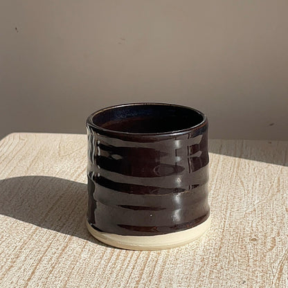 Black ceramic cup with wavy pattern on a textured surface