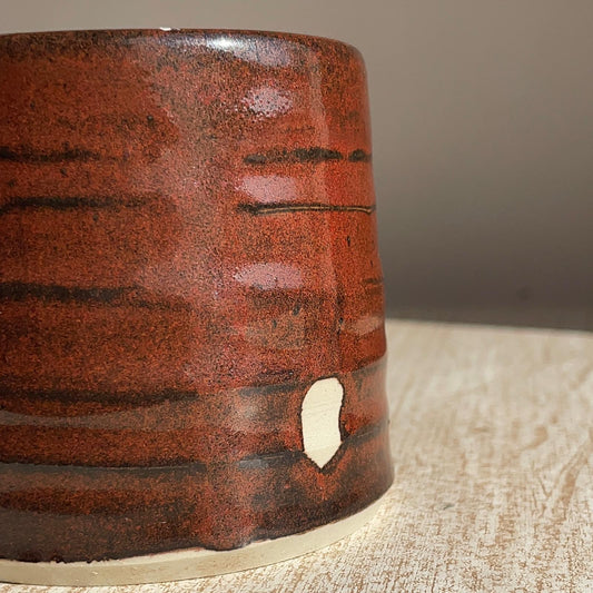 Close-up of a red cup with a textured surface on a wooden surface.