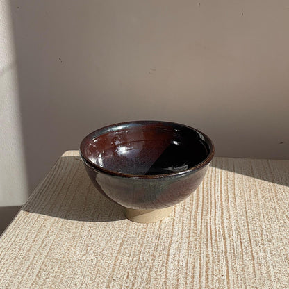 Brown ceramic bowl on a textured surface with a neutral background