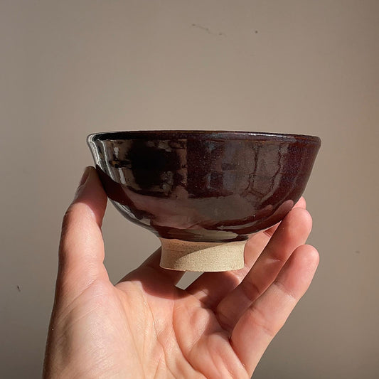 Hand holding a small brown ceramic bowl against a plain background