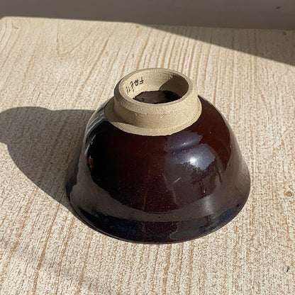 Brown ceramic bowl with a beige interior on a textured surface