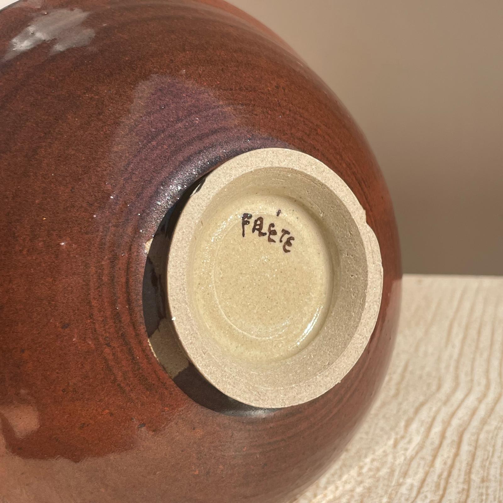 Close-up of the bottom rim of a ceramic bowl with 'FRÉTE' branding on a wooden surface.