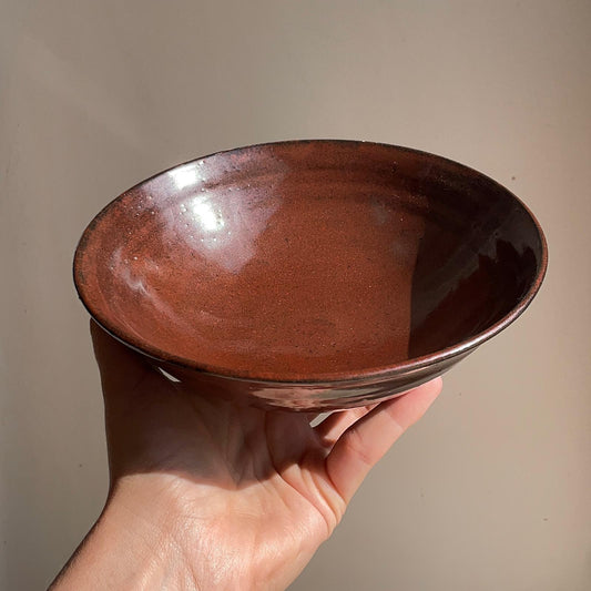 Hand holding a red ceramic bowl against a plain background