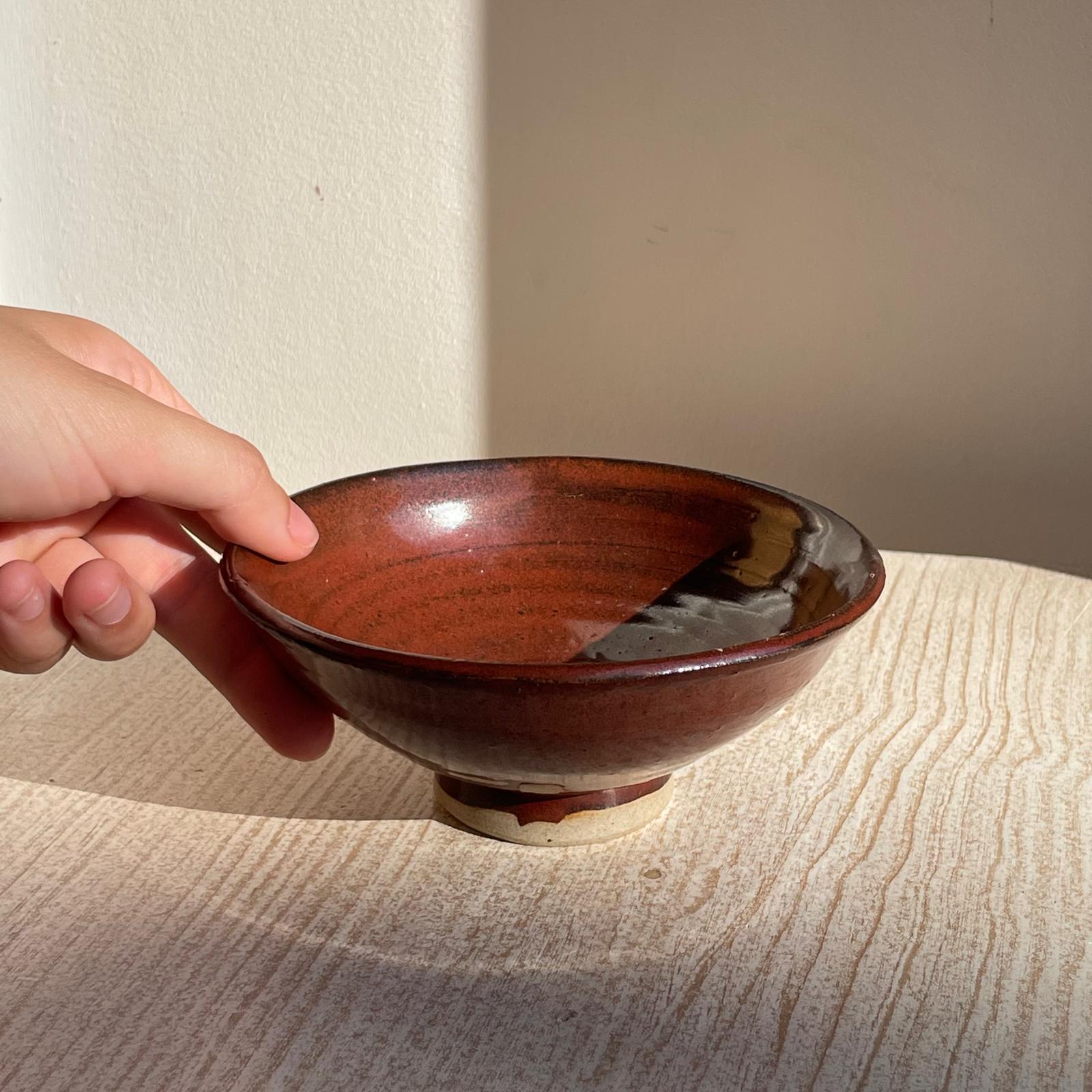 Hand holding a red ceramic bowl on a textured surface with a neutral background