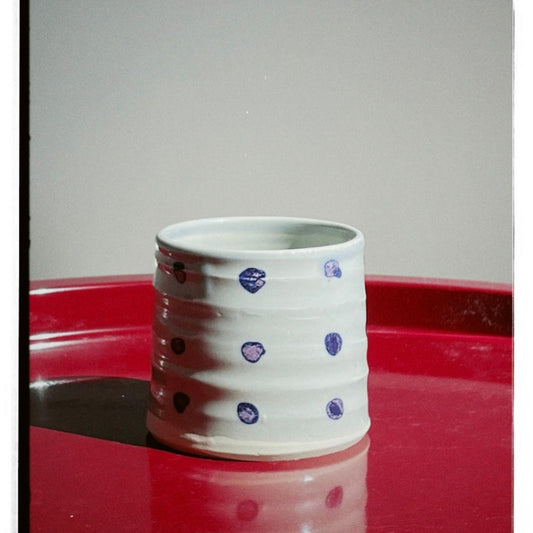 Ceramic cup with purple polka dots on a red surface