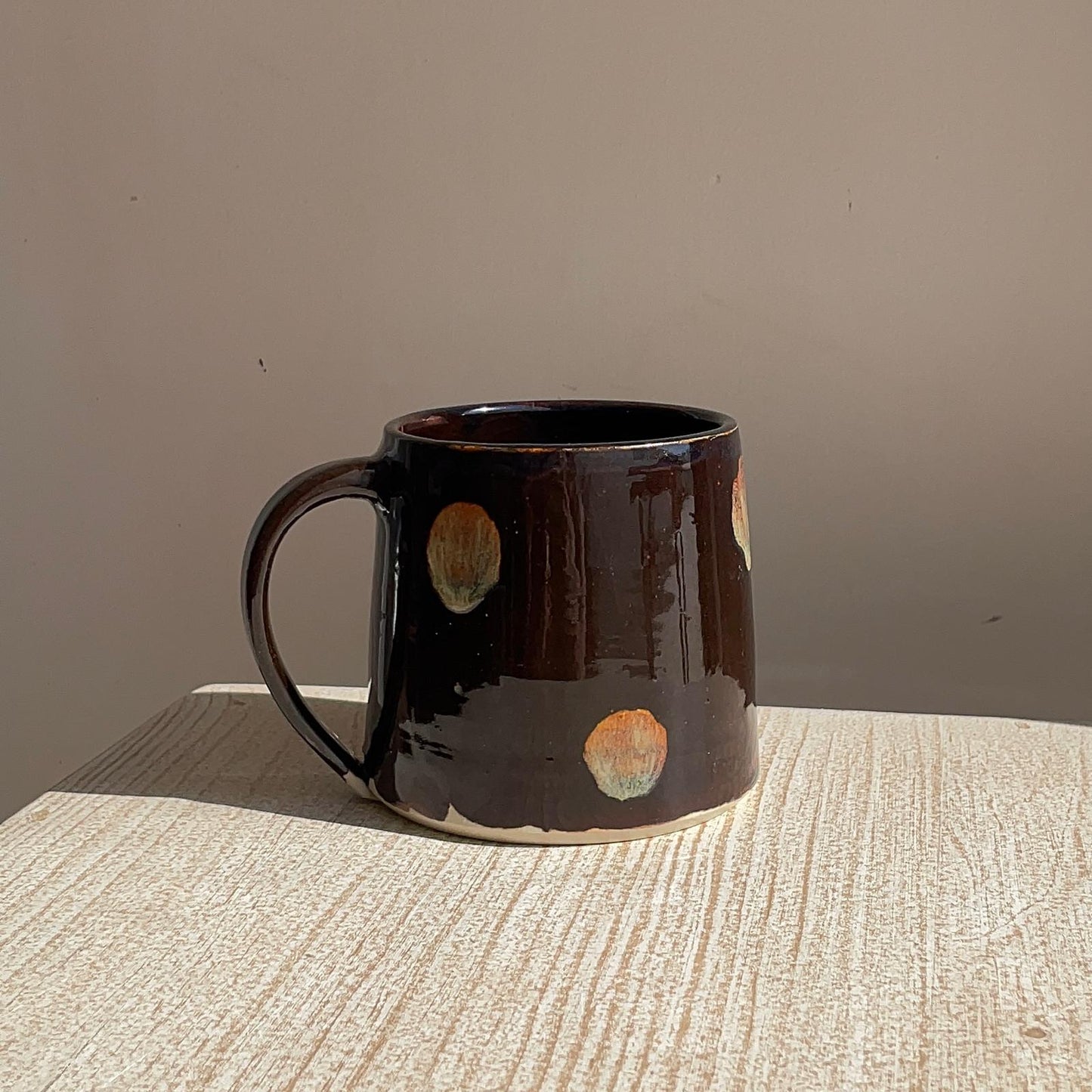 Brown ceramic mug with circular patterns on a textured surface and plain background
