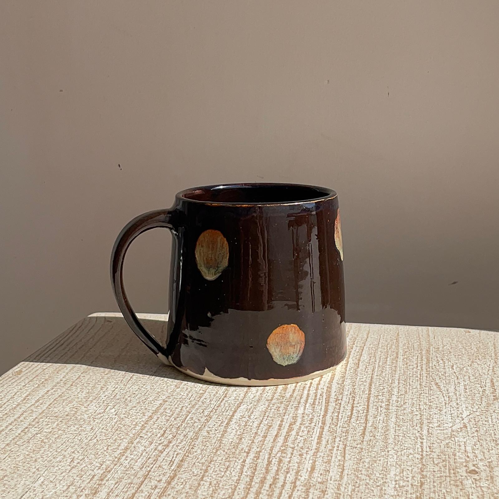 Brown ceramic mug with circular patterns on a textured surface and plain background