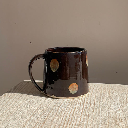 Brown ceramic mug with circular patterns on a textured surface and plain background