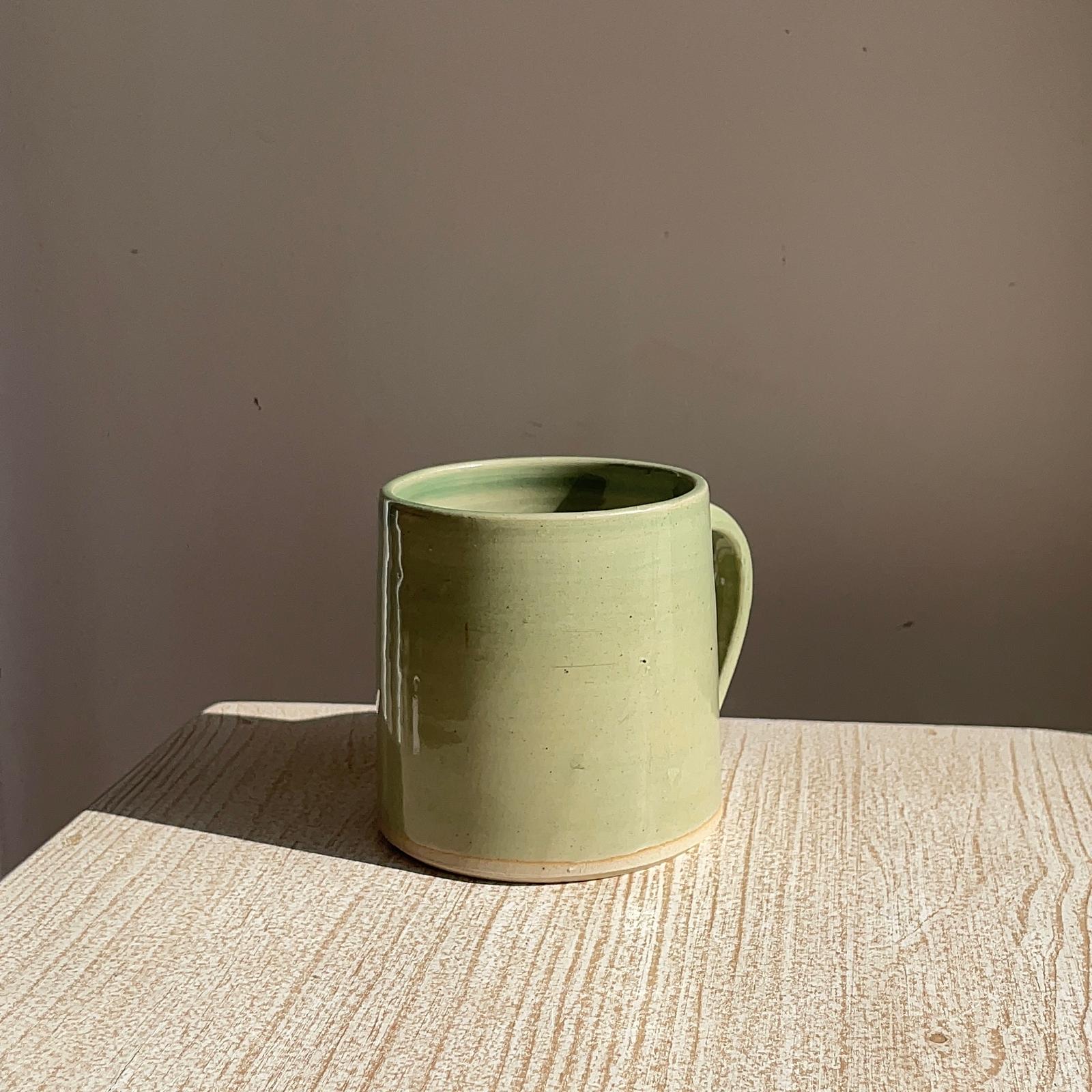 Green ceramic mug on a textured surface with a plain background
