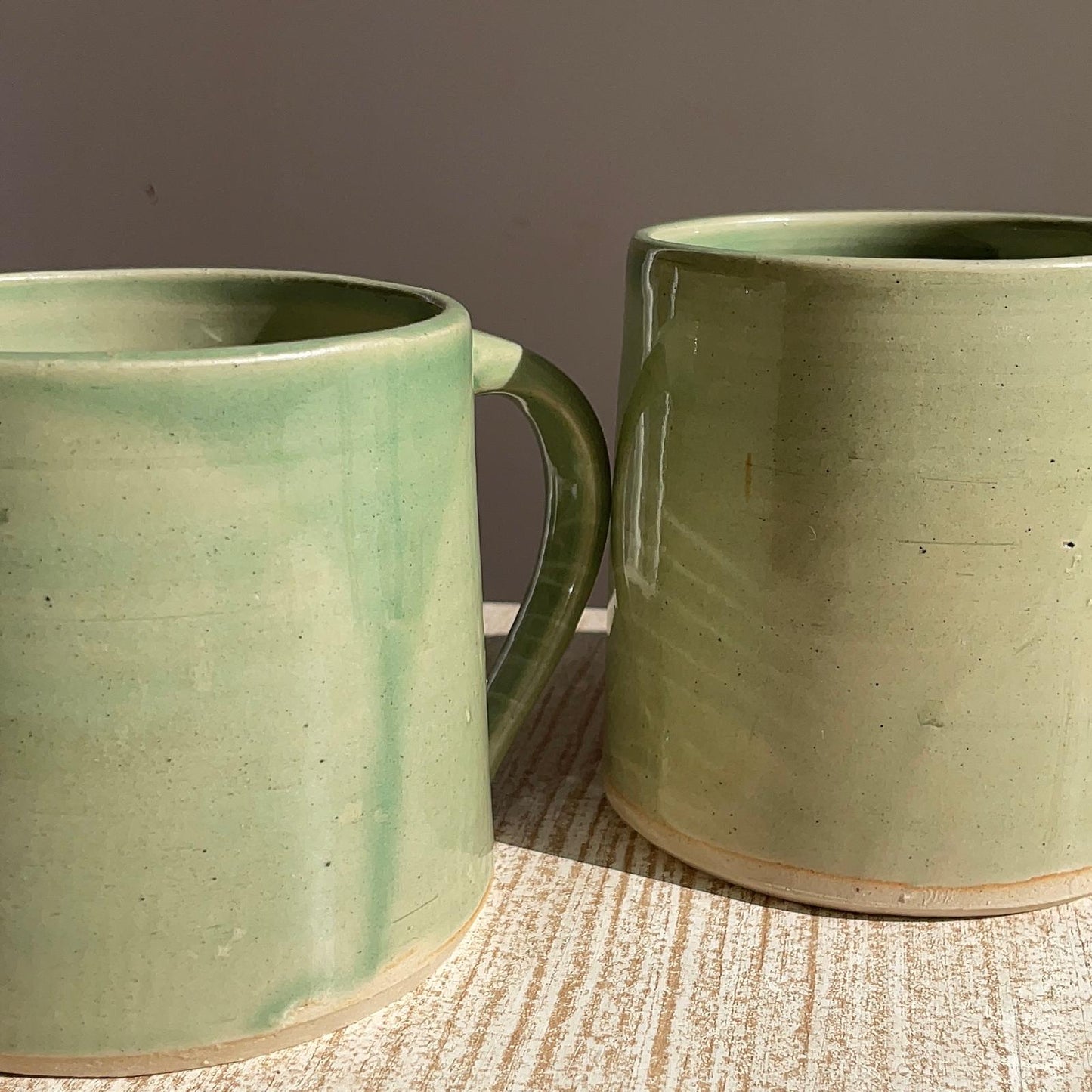 Two green ceramic mugs on a textured surface with a neutral background