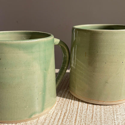 Two green ceramic mugs on a textured surface with a neutral background