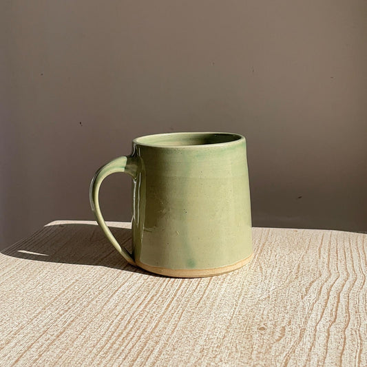 pale Green ceramic mug on a wooden surface with a brown background