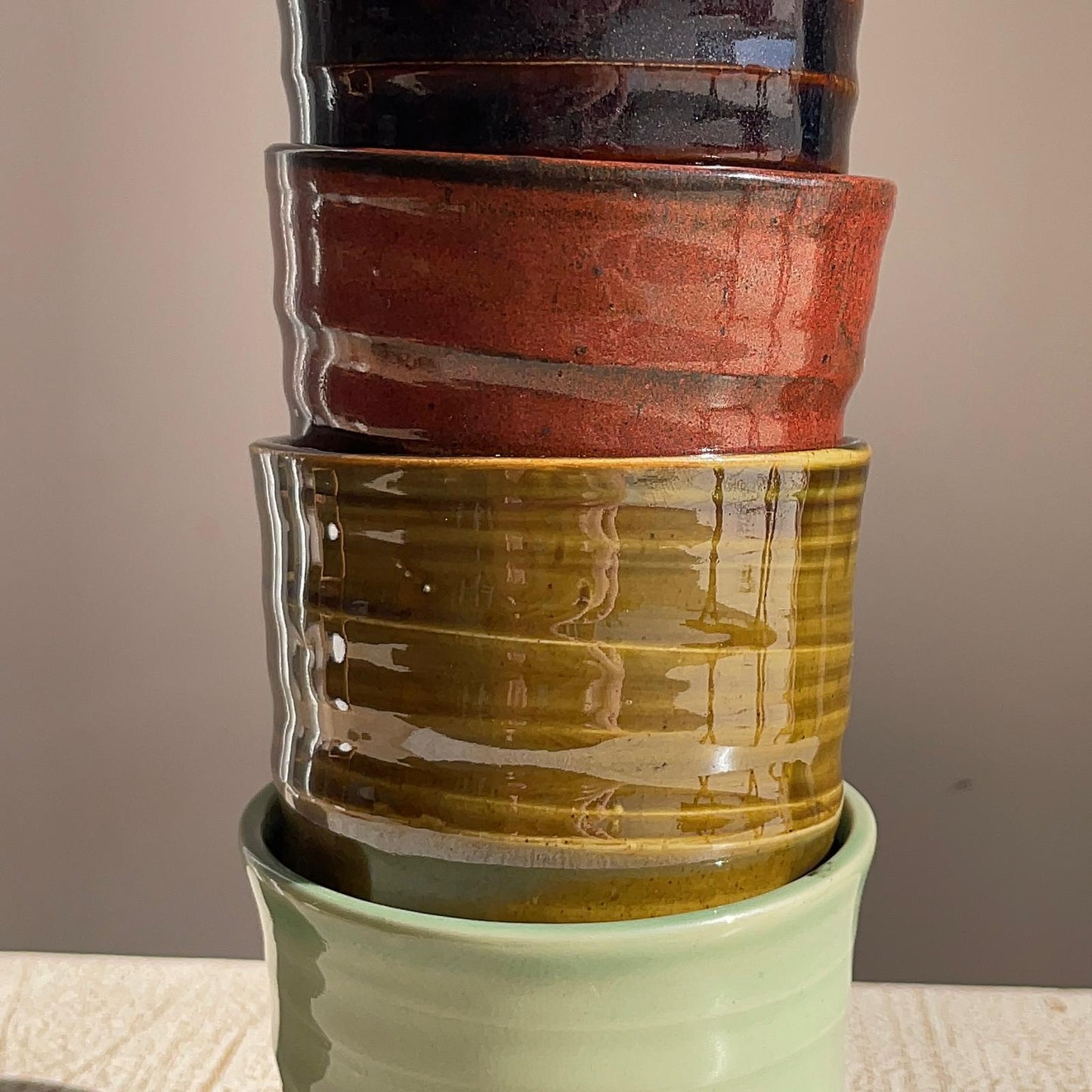 Stack of ceramic pots with different colored glazes on a neutral background