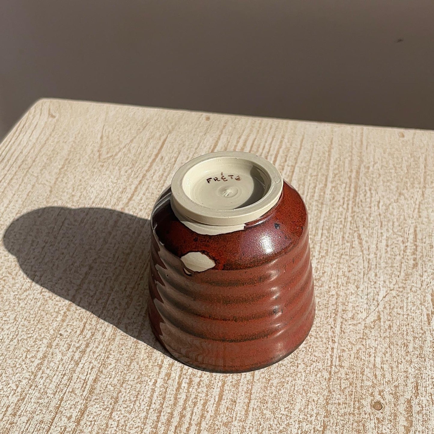 tenmoku red ceramic cup on a textured surface with a neutral background, focus on the foot