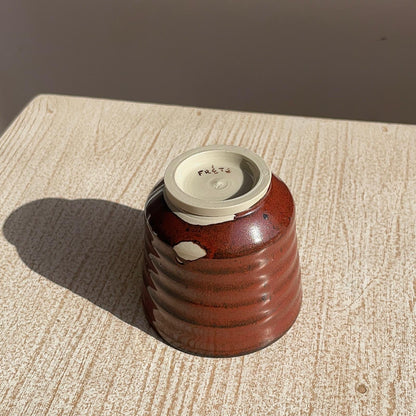 tenmoku red ceramic cup on a textured surface with a neutral background, focus on the foot