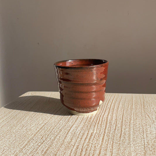 tenmoku red ceramic cup on a textured surface with a neutral background