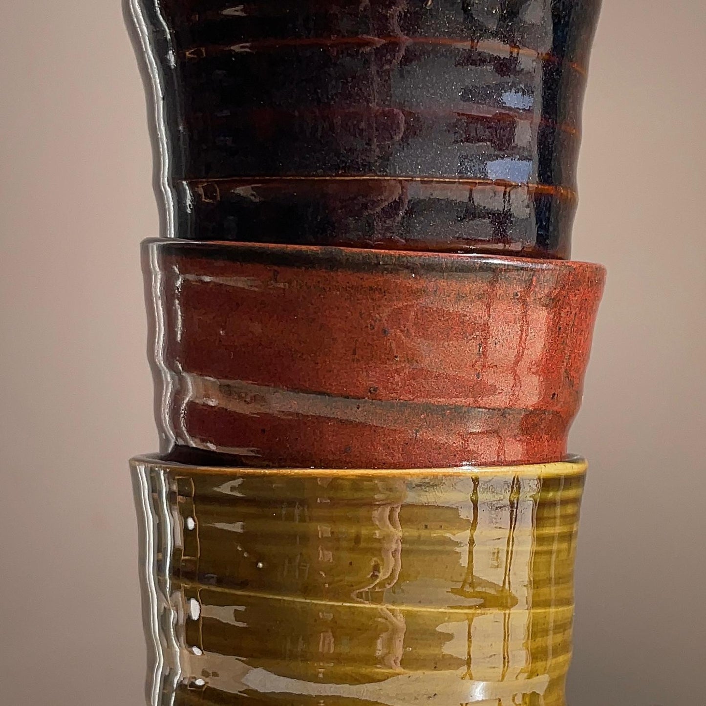 Stack of ceramic pots with different colored glazes on a beige background