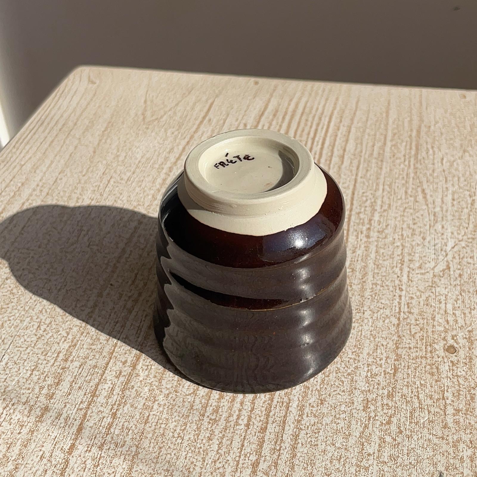 very dark brown ceramic cup upside dowm on a textured surface with a neutral background
close up on the foot