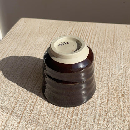 very dark brown ceramic cup upside dowm on a textured surface with a neutral background
close up on the foot