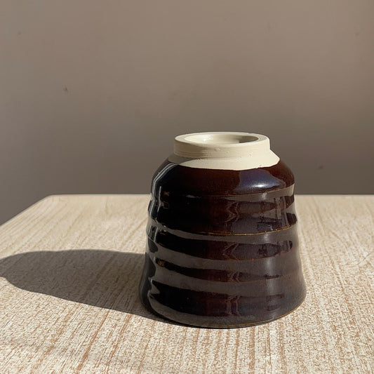 very dark brown ceramic cup upside down on a textured surface with a neutral background
