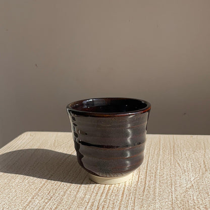 very dark brown ceramic cup on a textured surface with a neutral background