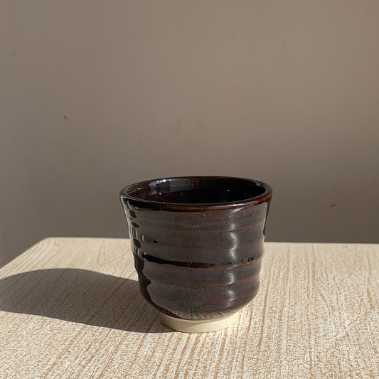 very dark brown ceramic cup on a textured surface with a neutral background