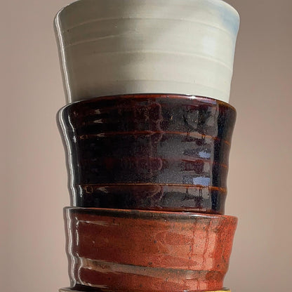 Stack of ceramic pots with different colored glazes on a neutral background