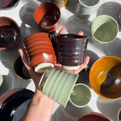 Hand holding a ceramic cups with various other mugs and bowls in the background
