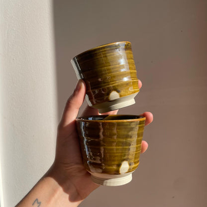 Hand holding two stacked ceramic cups with a brown glaze against a plain background