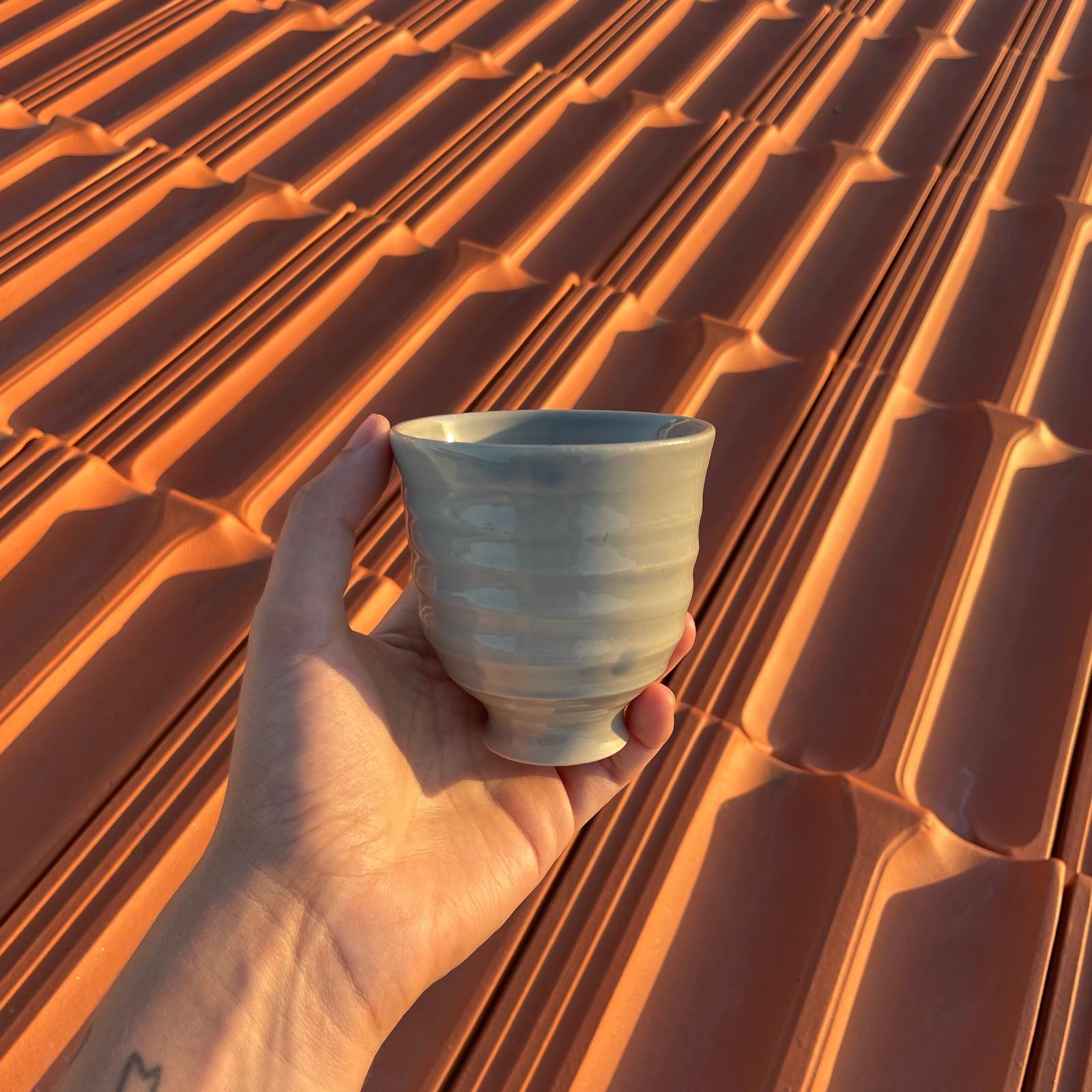 Hand holding a ceramic cup against a textured orange wall
