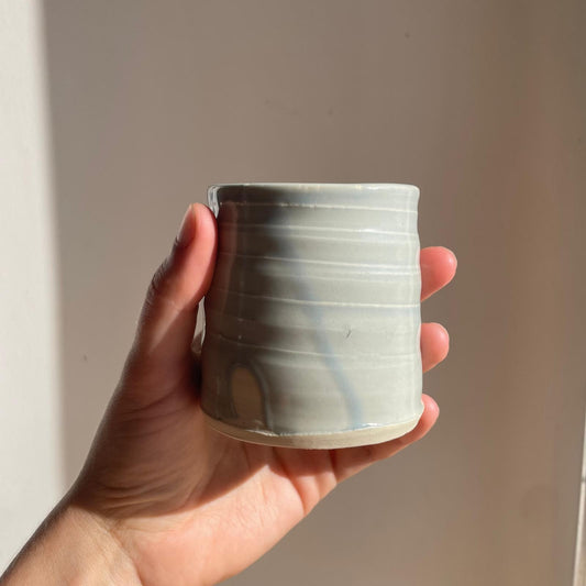 Hand holding a small ceramic cup against a plain background