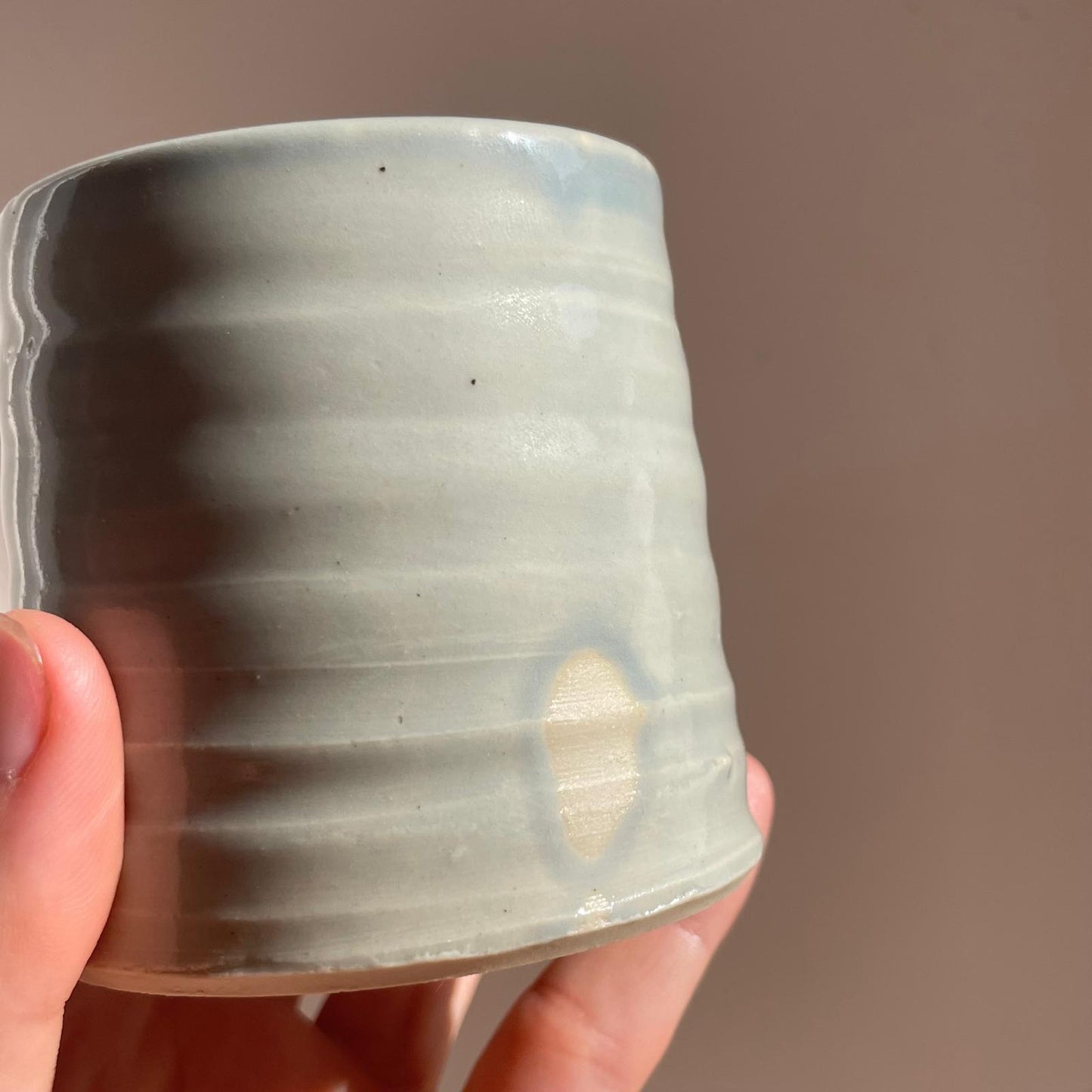 Hand holding a ceramic cup with a textured surface against a plain background