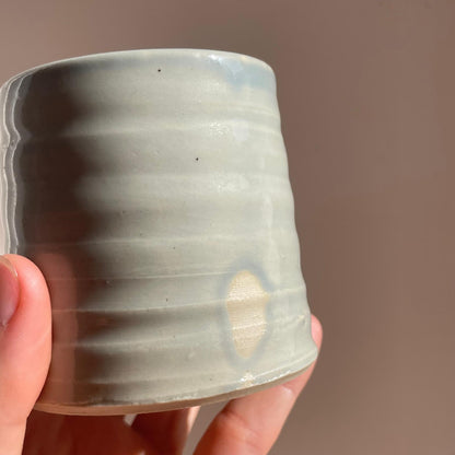 Hand holding a ceramic cup with a textured surface against a plain background