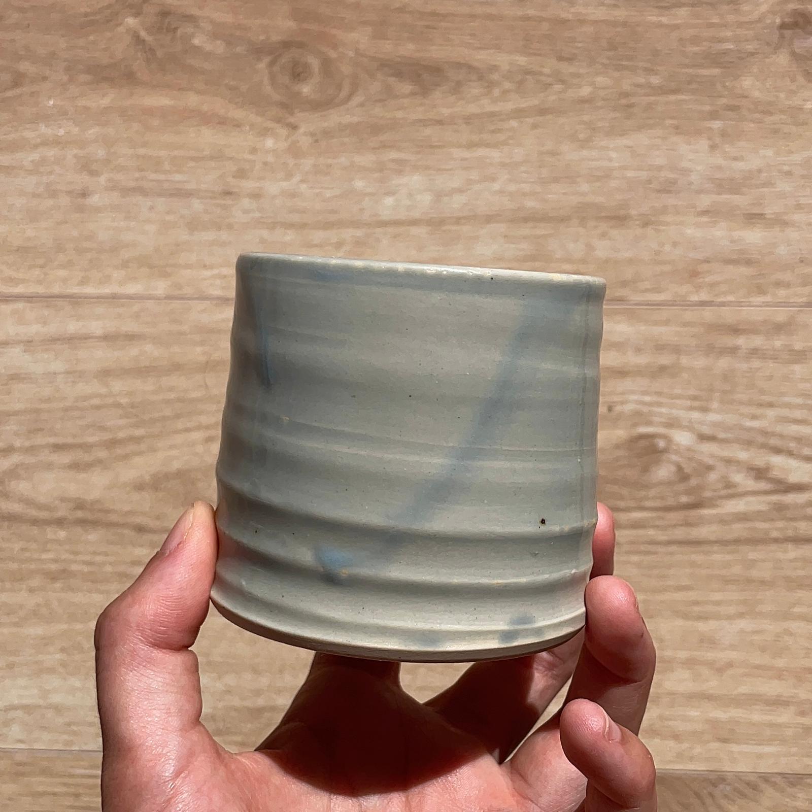 Hand holding a ceramic cup with blue accents on a wooden surface