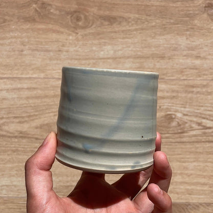 Hand holding a ceramic cup with blue accents on a wooden surface