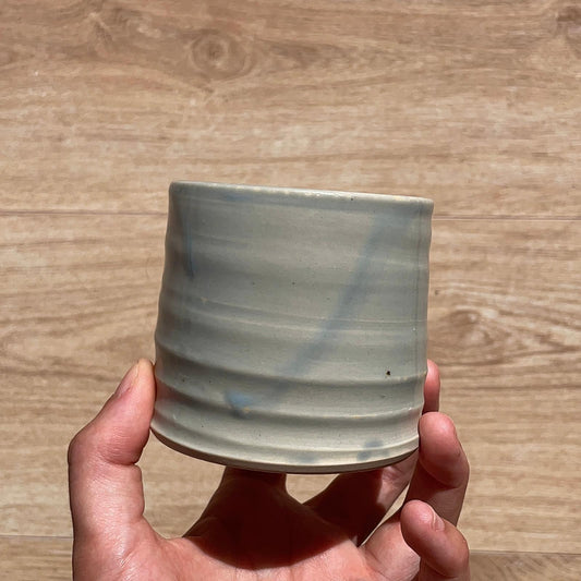 Hand holding a ceramic cup with blue accents on a wooden surface