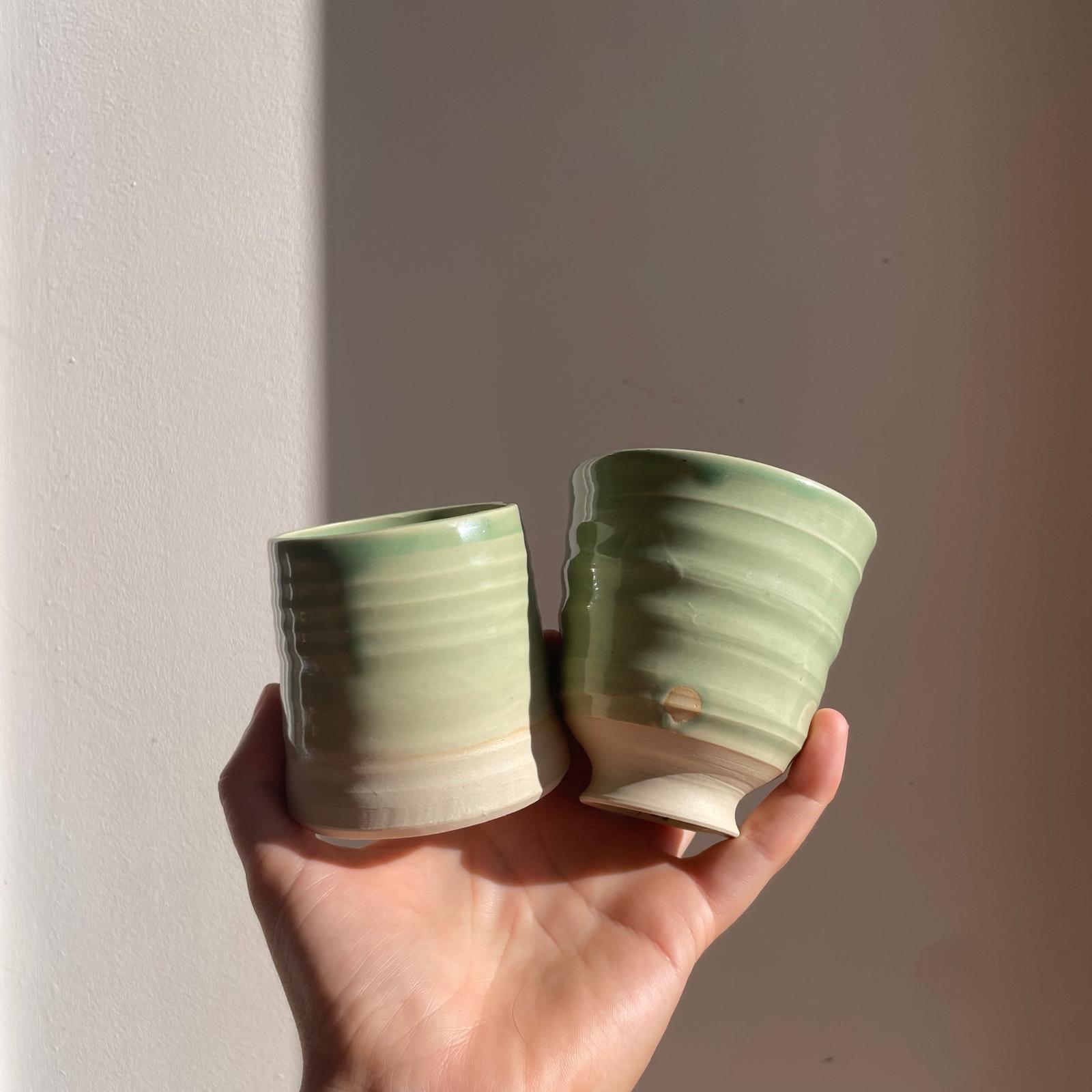 Two green ceramic cups held in a hand against a plain background