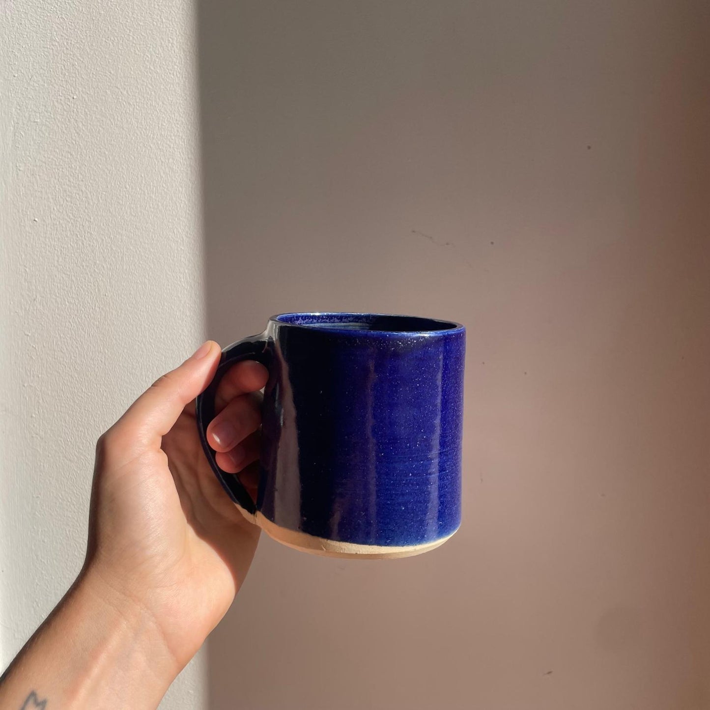 Hand holding a blue mug against a plain wall