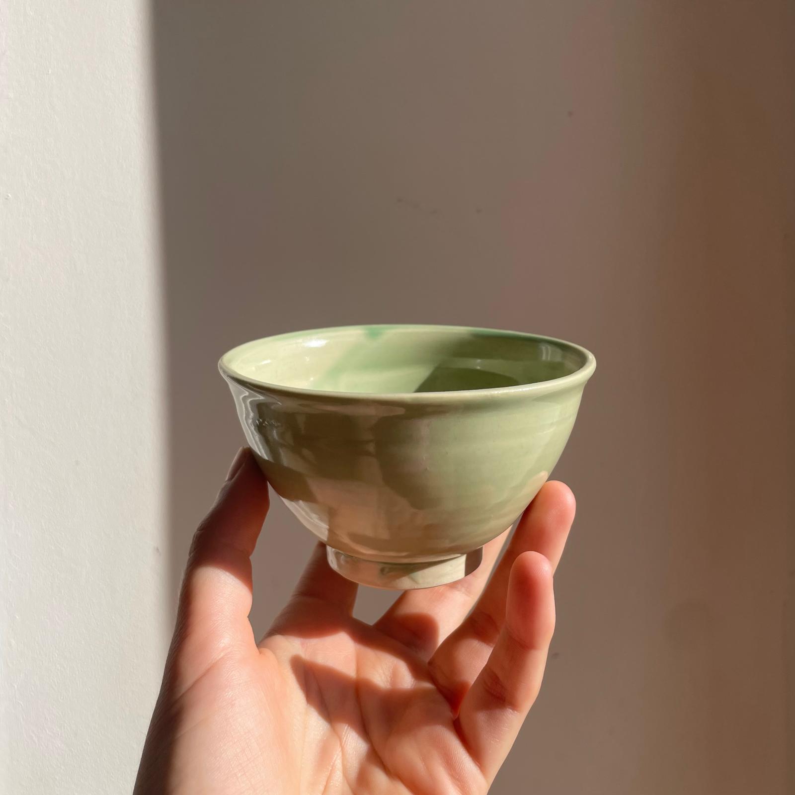 Hand holding a small green ceramic bowl against a plain background