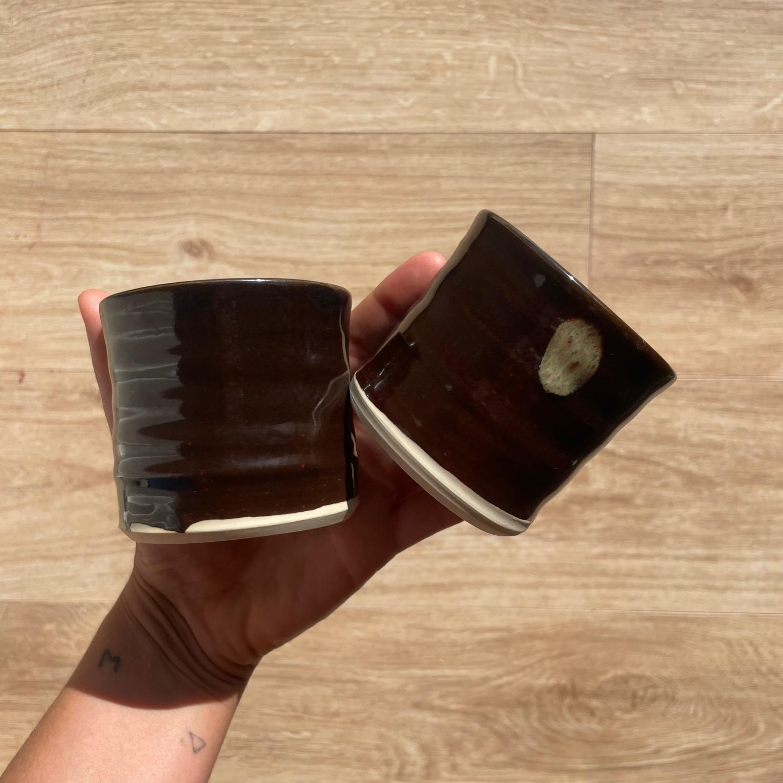 Two brown ceramic cups held in a hand against a wooden floor background